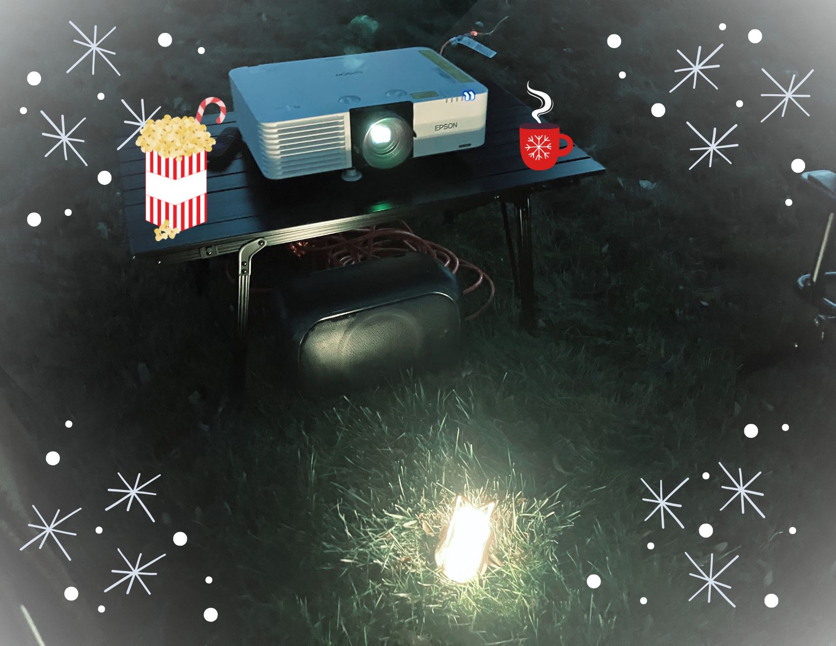 A projector on a table with a cartoon hot cocoa mug and a popcorn